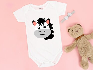 Weißer Baby-Body mit großem Zebrakopf-Plott, auf rosa Hintergrund mit Haarband und Teddybär als Requisite