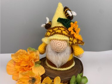 Yellow and brown crocheted amigurumi gnome with bees and a sunflower on a wood slice