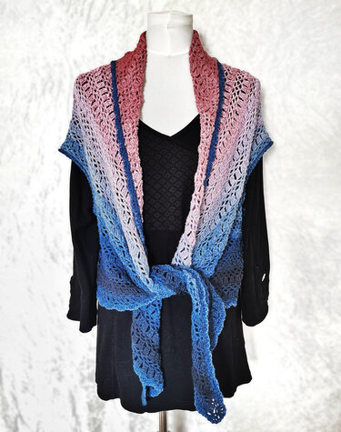 Crocheted gradient shawl in pink-to-blue ombre with lace stitch, tied at the front on a mannequin.