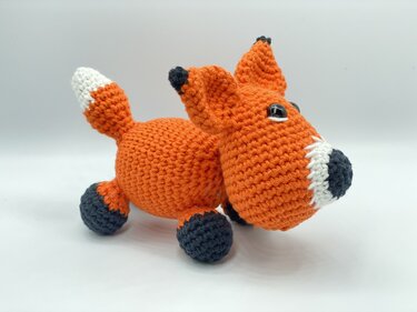 Gehäkelter Amigurumi-Fuchs orange und weiß mit dunkelgrauen Pfoten und schwarzen Augen