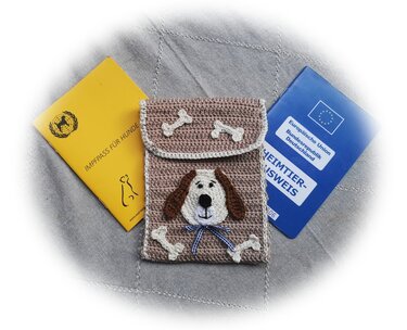 Beige gehäkelte Hülle mit Hundegesicht und Knochen-Applikationen, daneben Impfpass und Heimtierausweis