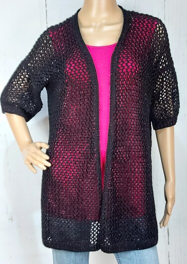 Schwarze offene Strickjacke mit Ajour-Lochmuster über pinkem Top an Schaufensterpuppe