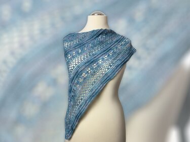 Blue crochet triangle shawl draped on a mannequin showing open lacework and textured stripe sections.