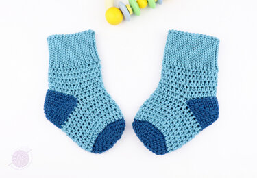 Flat-lay of textured light-blue crochet baby socks showing ribbed cuff and dark-blue heel and toe