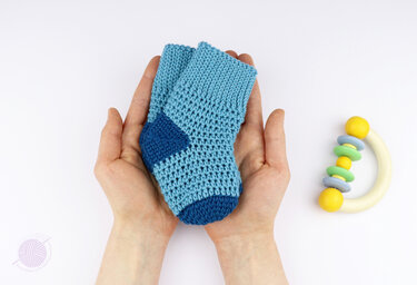 Paar gehäkelter Babysocken in hell- und dunkelblau in offenen Händen