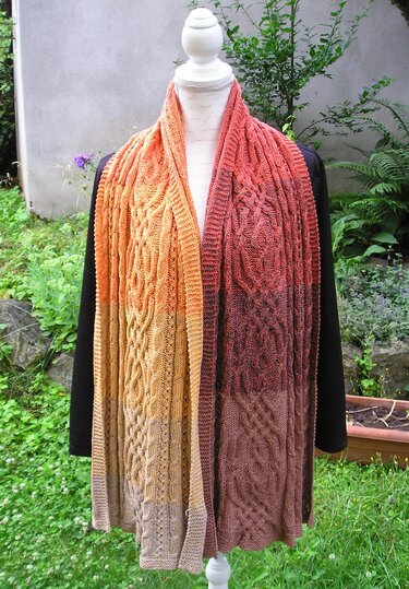Mannequin trägt langen gestrickten Schal mit Zopfmuster und gelb-orangem bis braunem Farbverlauf