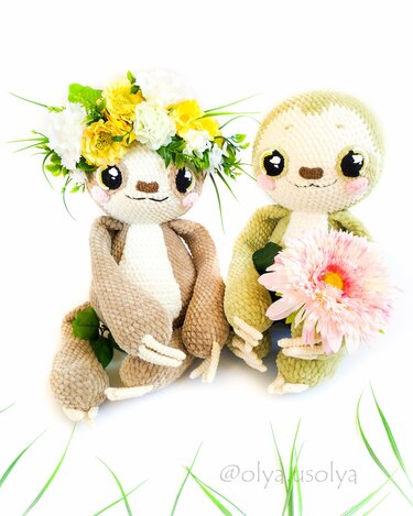 Zwei gehäkelte Faultiere, eines mit Blumenkranz, das andere mit rosa Blüte