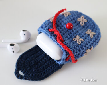 Compact blue crochet earbud cozy with red cord and bead closure beside white earbuds