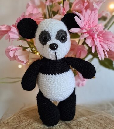 Einfach gehäkeltes schwarz-weißes Panda-Amigurumi vor rosa Blumen