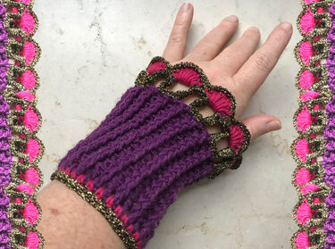 Dunkelviolette gehäkelte Armstulpe mit pink-goldener Wellenkante an einer Hand