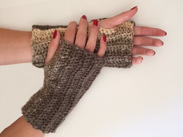 Gehäkelte fingerlose Handschuhe in Braun- und Beigetönen an Händen