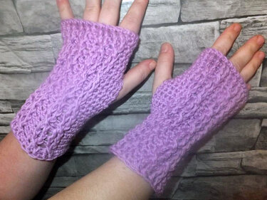 Lila gehäkelte, fingerlose Armstulpen mit Zopfmuster an Händen getragen