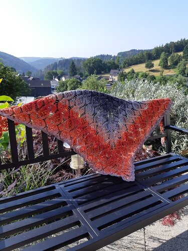 Lightweight lacy shell-stitch crochet triangle shawl with orange-to-gray gradient draped over a bench