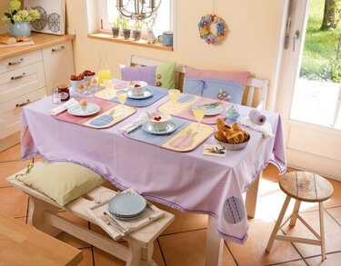 Tisch mit pastellfarbener Tischdecke, bunten Platzsets und Kissen, gedeckt zum Frühstück