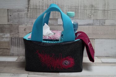 Rechteckiger Stoff-Organizer mit türkisfarbenen Henkeln und roter Federstickerei, auf Holzablage platziert.