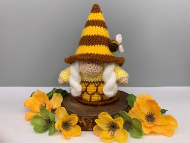 Crochet gnome with yellow-brown striped hat, white braids, honeycomb skirt, bee accent