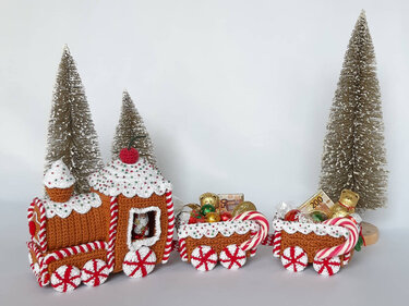 Gehäkelter Weihnachtszug-Amigurumi mit zwei gefüllten Waggons vor dekorativen Tannen
