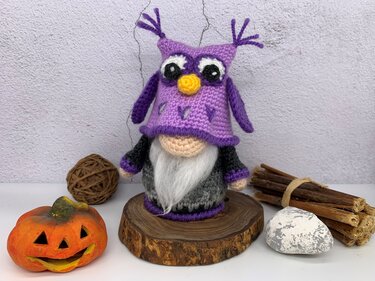 Crocheted gnome with purple owl hat and white beard on a wooden slice with seasonal accents.