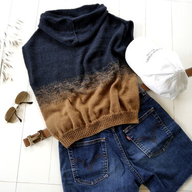 Flat lay of a knitted sleeveless cowl neck top in a blue-to-brown gradient with denim shorts, belt, and sunglasses.