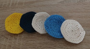 Fünf runde Häkel-Pads in verschiedenen Farben auf Holz