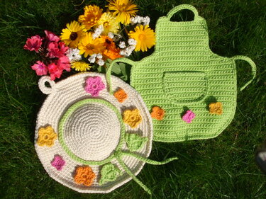 Zwei gehäkelte Topflappen auf Gras: runder beiger Untersetzer mit Blumen und grüner Topflappen mit Tasche