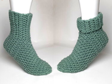 Paar gehäkelter knöchelhoher Socken in Salbeigrün auf Schaufensterbeinen