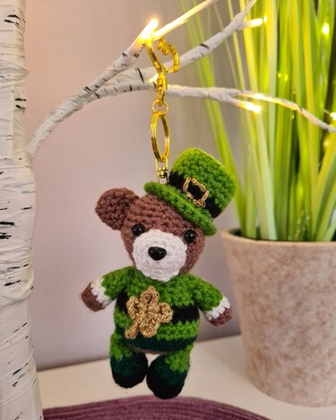 Gehäkelter Amigurumi-Teddybär als Schlüsselanhänger mit grünem Zylinderhut, Kleeblatt und grün-schwarzem Outfit.