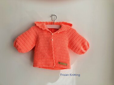 Coral crocheted baby jacket with ruffle collar and pearl buttons on a hanger
