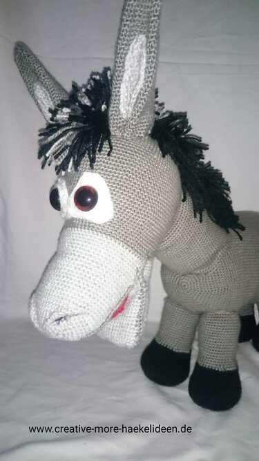 Gehäkelter grauer Amigurumi‑Esel mit schwarzer Mähne und dunklen Augen, dreiviertelansicht