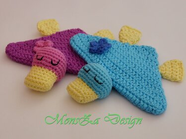 Zwei gehäkelte Schmusetücher für Babys mit schlafenden Tierköpfen in Blau-Gelb und Rosa-Gelb auf hellem Hintergrund.