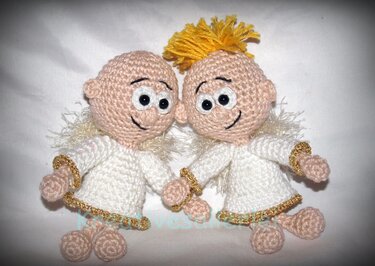 Zwei gehäkelte Engelchen in weißen Kleidern mit goldener Kante und flauschigen Flügeln, die Händchen halten