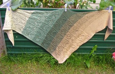 Gestricktes Dreieckstuch in Beige- und Grüntönen mit durchbrochenem Spitzenmuster, aufgehängt an einer grünen Wand