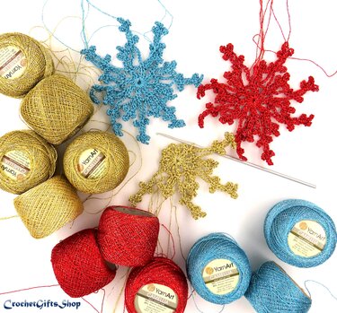 Gold, red, and blue metallic crochet snowflake ornaments with matching thread balls and a crochet hook on a white background
