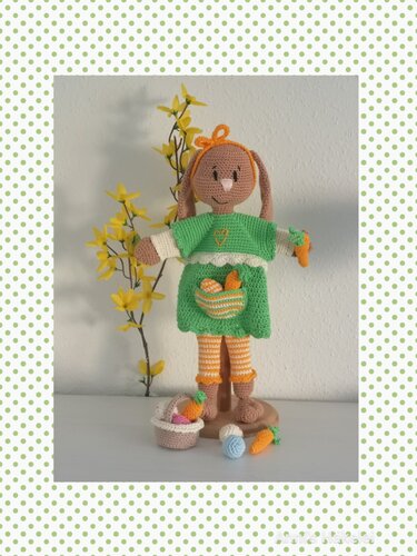 Amigurumi-Osterhase im grünen Kleid auf Holzständer mit Körbchen, Ostereiern und Karotten