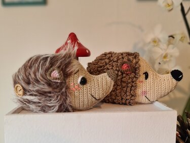 Zwei handgehäkelte Igel‑Amigurumi nebeneinander auf weißer Fläche, einer flauschig, einer mit Noppenstichen.