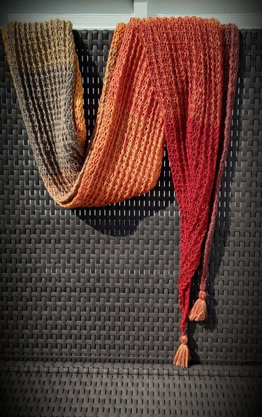 Langer gehäkelter Ombre-Schal in Braun-, Orange- und Rottönen mit Strukturmuster und Quasten, drapiert