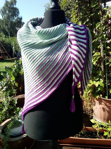 Gehäkeltes Dreieckstuch in Mint, Weiß und Lila mit diagonalem Streifenmuster und Quaste auf schwarzer Schneiderpuppe im Garten