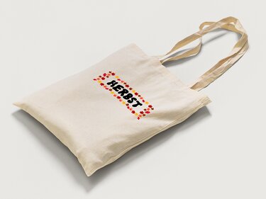 Beige Baumwolltasche mit schwarzem Schriftzug 'HERBST' in einem rechteckigen Rahmen aus roten, orangen und gelben Herbstblättern