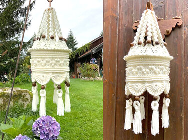 Cremefarbene, gehäkelte Hängedekoration mit aufwendigen Mustern, Holzperlen und langen Quasten vor Holzwand und Garten