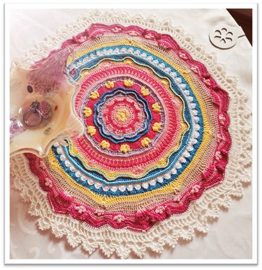 Häkelmandala in Pink, Gelb und Blau mit cremefarbener Spitzenkante auf Tischdecke