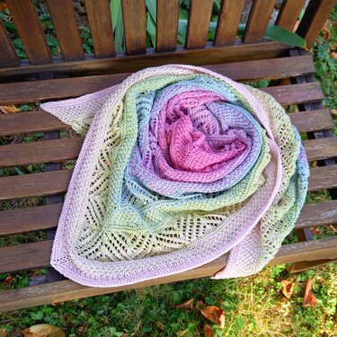 Gestricktes Dreieckstuch mit pastellfarbenem Farbverlauf und Ajourrand auf einer Holzbank