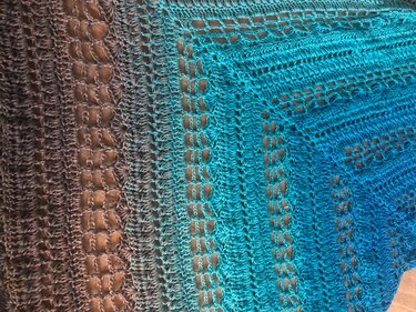 Nahaufnahme eines gehäkelten Dreieckstuchs mit türkisem bis braunem Farbverlauf und offenem Lochmuster