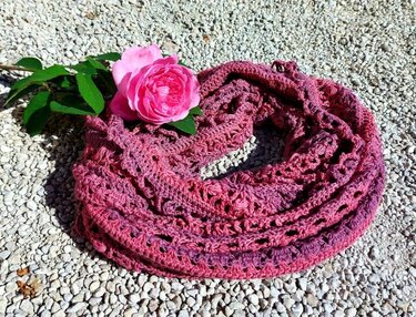 Crocheted pink and purple variegated lace scarf with a pink rose on gravel.