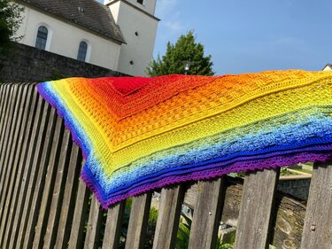 Gehäkeltes Dreieckstuch mit Regenbogen-Farbverlauf auf Holzzaun