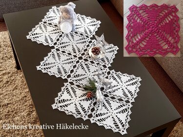 Weißer gehäkelter Läufer aus verbundenen Quadraten auf dunklem Couchtisch mit silberner Weihnachtsdekoration und Tannenzweig