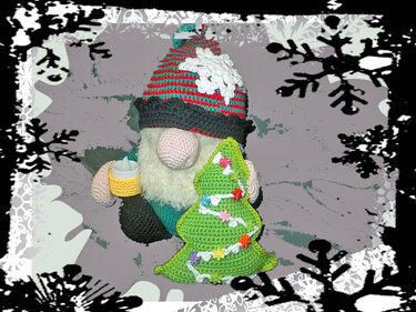 Gehäkelter Weihnachtswichtel mit gestreifter Mütze, weißem Bart und rosa Nase, der eine Kerze hält, neben einem gehäkelten grünen Tannenbaum mit bunten Verzierungen.