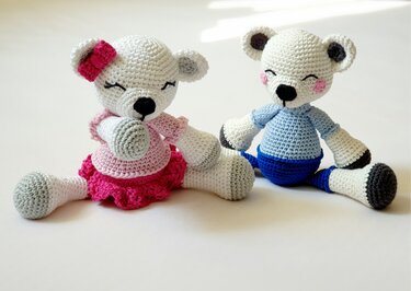 Zwei sitzende gehäkelte Amigurumi-Teddybären, einer rosa mit Schleife, einer blau mit Pullover