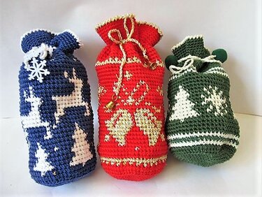 Drei gehäkelte Weihnachts-Geschenksäckchen in Blau, Rot und Grün mit Rentier-, Tannenbaum- und Glockenmotiven