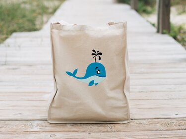 Beiger Stoffbeutel mit stilisiertem blauem Walmotiv und schwarzer Wasserfontäne