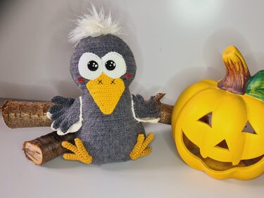 Handgehäkelter Vogel mit weißem Bommel neben herbstlicher Kürbisdekoration